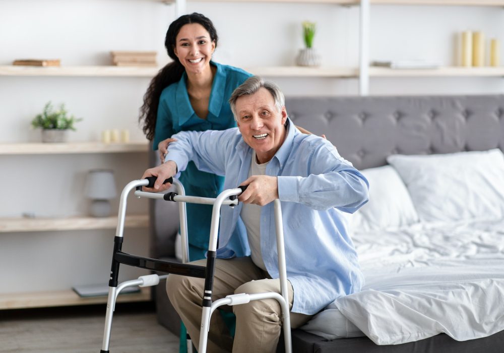 female-nurse-helping-elderly-male-with-walking-frame-stand-up-from-bed-at-home-professional-care.jpg